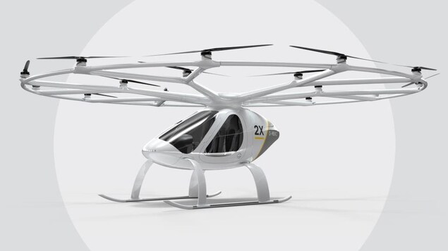 Une capture d'écran montrant le Volocopter 2X, qui ressemble à un gros drone muni d'une quinzaine d'hélices. Une capture d'écran montrant le Volocopter 2X, qui ressemble à un gros drone muni d'une quinzaine d'hélices.