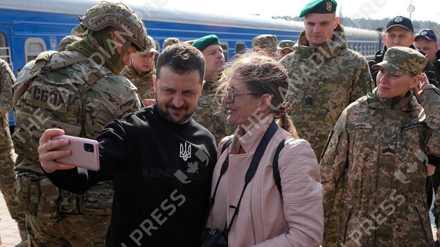 Entouré de militaires, le président ukrainien Volodymyr Zelensky tient un téléphone cellulaire au bout de son bras.