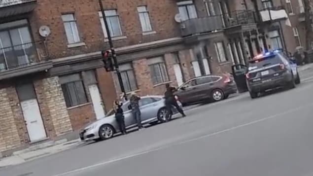 Des policiers retranchés derrière une voiture pointent leurs armes vers un autre véhicule.
