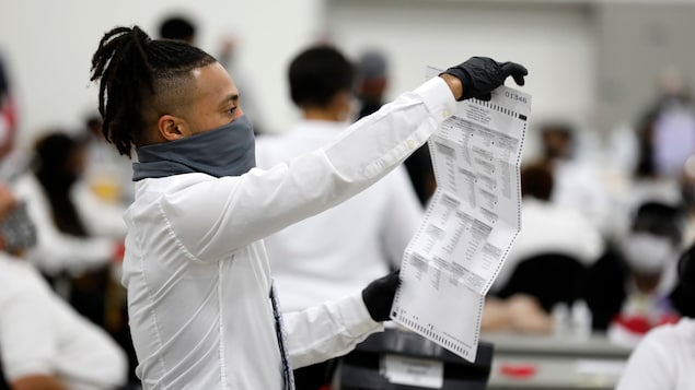 Un travailleur d'élection tient un bulletin de vote à la hauteur de ses yeux.