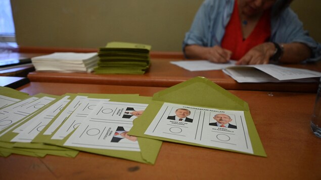 Une femmes écrit sur un papier près de bulletins de vote à l'image des candidats à la présidence turque.