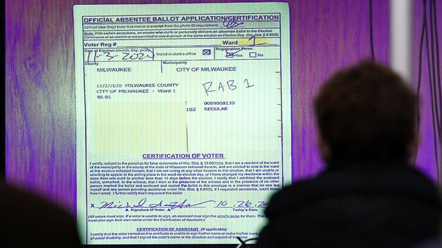 Des observateurs regardent sur un écran géant le document de certification d'une demande de vote postal lors de la vérification manuelle des votes à Milwaukee, au Wisconsin.