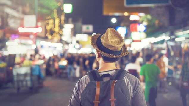 Un jeune touriste, de dos, visite une ville asiatique.
