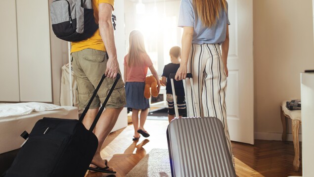 Deux adultes et deux enfants photographiés de dos, sortant de leur domicile. Les deux adultes tirent des valises.