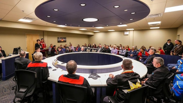 Deux magistrats assis d'un côté d'une grande table circulaire. En face d'eux se trouvent quelques dizaines de personnes assises dans des fauteuils. Deux magistrats assis d'un côté d'une grande table circulaire. En face d'eux se trouvent quelques dizaines de personnes assises dans des fauteuils.