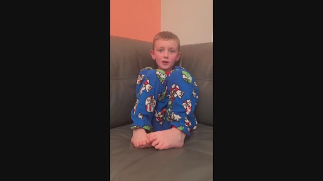 Un jeune garçon en pyjama de Mario Bros sur un divan gris.