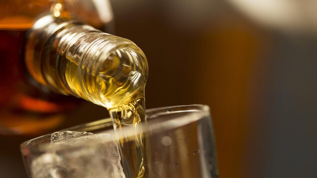 Du whisky est versé sur de la glace dans une verre.