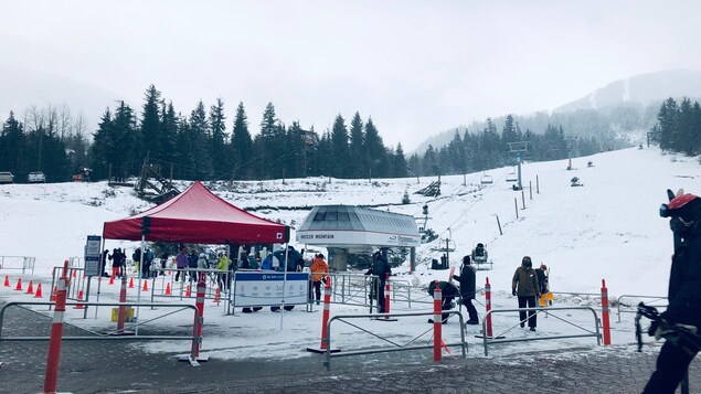 Une dizaine de skieurs attendent en file devant le remonte-pente qui les amènera au sommet d'une montagne enneigée.