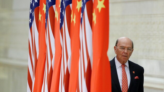 Wilbur Ross devant des drapeaux américains et chinois. 