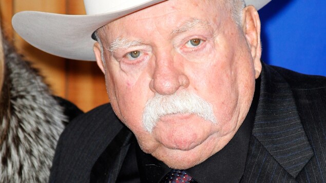 Un homme à moustache portant un chapeau de cowboy blanc prend la pose.