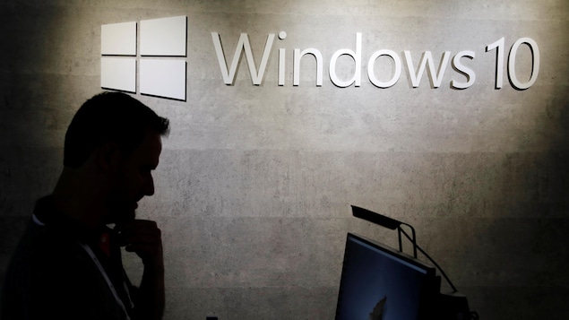 Un homme regarde un ordinateur avec le logo de Windows 10 en arrière-plan.