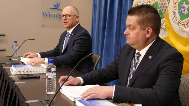 Deux hommes se tiennent devant un micro, derrière les drapeaux de la ville de Winnipeg, le 8 février 2023. 