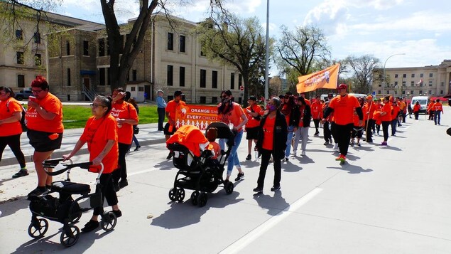 Des personnes vêtues de chandail orange défilent sur le boulevard Memorial à Winnipeg.