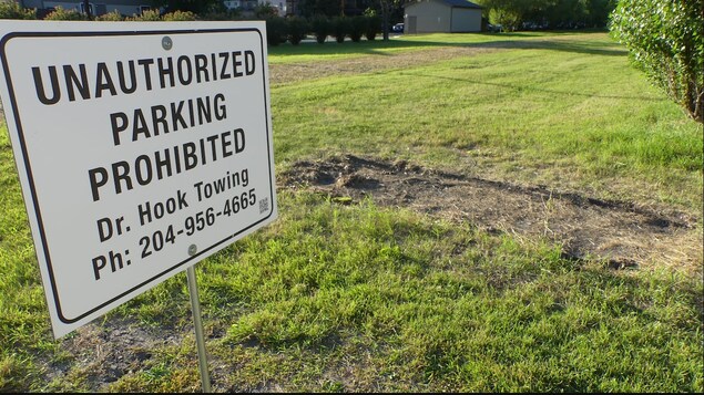 Une pancarte interdisant le stationnement sur un terrain vert dans lequel une voiture a laissé une démarcation. 