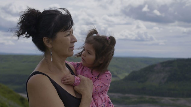 Diane Abel tient dans les bras sa petite fille en regardant le paysage du futur barrage.