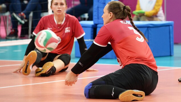 Une femme assis sur le terrain de volleyball qui fait une manchette à un ballon.