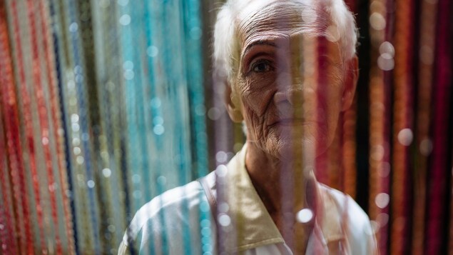 Une dame âgée regarde à travers un rideau multicolore.