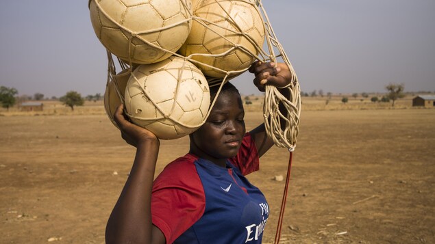 Une jeune femme porte des ballons de soccer sur sa tête.
