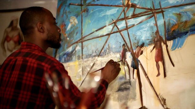 L'artiste Xavier Mutshipayi peignant un tableau, dans son atelier.