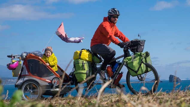 Xavier Pasche à vélo avec une de ses filles dans la charrette.