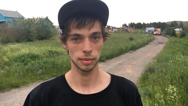 Un homme se trouve à l'extérieur. Derrière lui, on remarque des camions de sécurité puisqu'on se trouve tout près des lieux d'un incendie. Un homme se trouve à l'extérieur. Derrière lui, on remarque des camions de sécurité puisqu'on se trouve tout près des lieux d'un incendie.