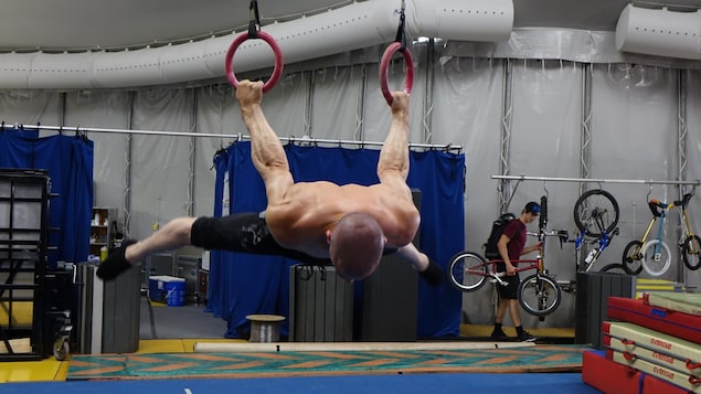 L'image montre un athlète de cirque suspendu à des anneaux. L'image montre un athlète de cirque suspendu à des anneaux.