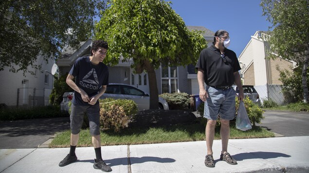 Yanny et Jacques Mignault, qui porte un masque, se tiennent à distance, sur le trottoir d'un quartier résidentiel.