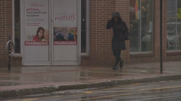 Une femme portant un imperméable marche sous la pluie en se protégeant la tête