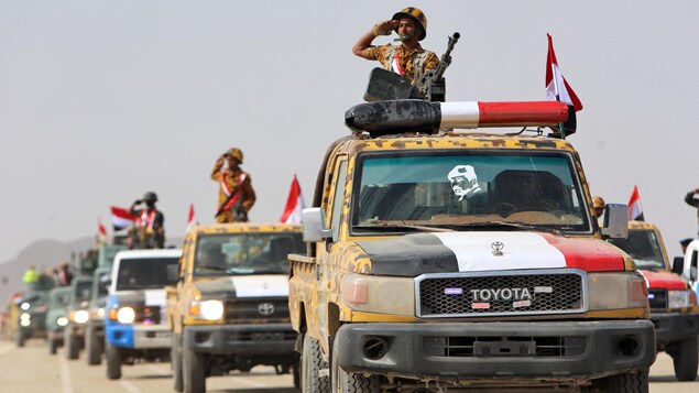 Des combattants yéménites font un salut depuis la plage arrière d'un véhicule.