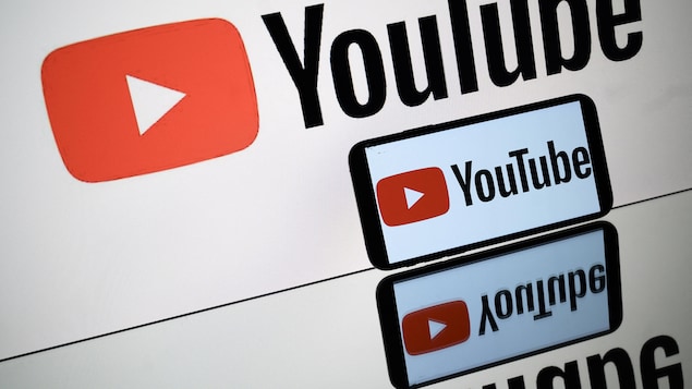 Le logo de YouTube apparait sur un écran géant en arrière-plan d'un téléphone qui affiche le même logo.