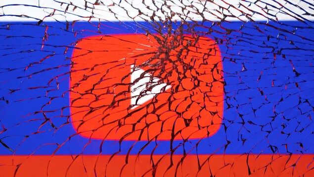 Le logo de YouTube, placé sur un drapeau russe, vu à travers une vitre brisée. 