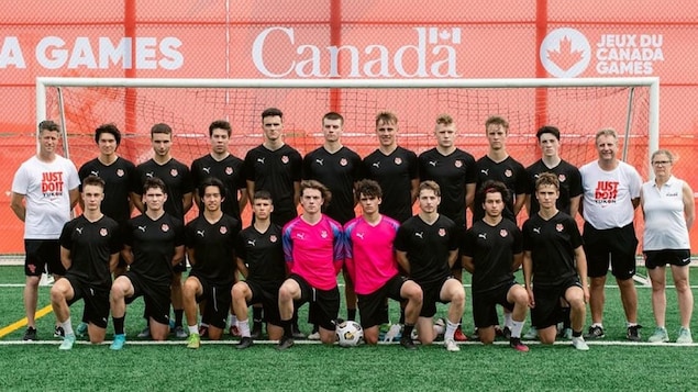 Des joueurs de soccer de l'équipe masculine du Yukon posent ensemble devant un but sur un terrain synthétique.