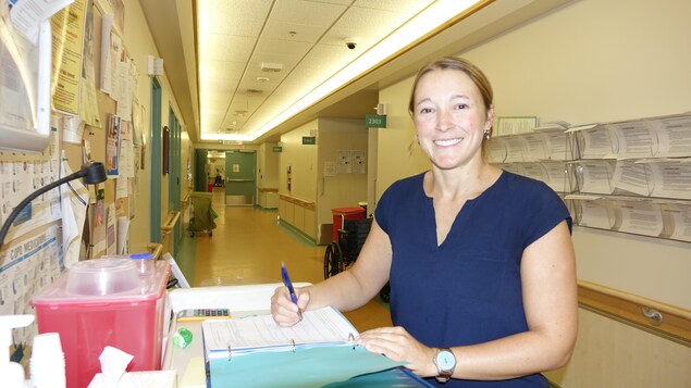 Une femme dans un couloir d'hôpital sourit à la caméra.