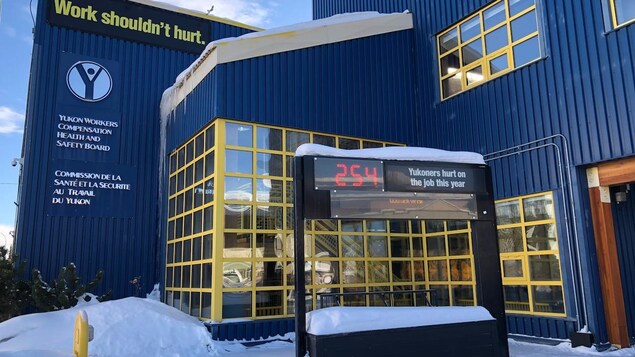 Front view of theThe Yukon Workers’ Compensation Health and Safety Board building. It is winter, with snow on the ground, on the roof and window ledges. The board holds a digital count of accidents in the workplace near the entrance of the building which says "254 Yukoners hurt on the job this year",