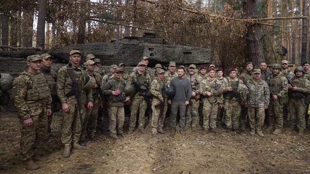 Volodymyr Zelensky pose devant un tank, entouré de soldats.