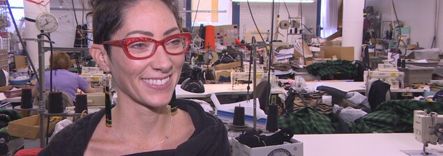 Andréanne Dandeneau est dans son atelier de vêtements, Il y a des machines à coudre, des boîtes et des tissus. Andréanne Dandeneau est dans son atelier de vêtements, Il y a des machines à coudre, des boîtes et des tissus.