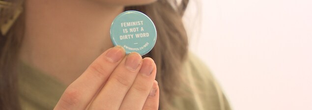 Un petit macaron bleu où il y est écrit en blanc le texte suivant : « féministe n'est pas un gros mot ». Un petit macaron bleu où il y est écrit en blanc le texte suivant : « féministe n'est pas un gros mot ».