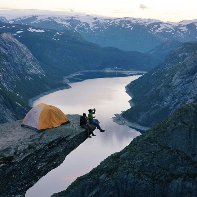 Deux personnes se tiennent au bout d'un pic rocheux sur lequel ils ont installé leur tente à Trolltunga en Norvège.