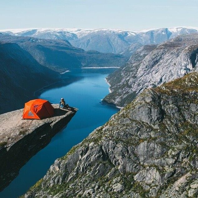 Une personne est assise au bout d'un pic rocheux sur lequel elle a installé leur tente à Trolltunga en Norvège.