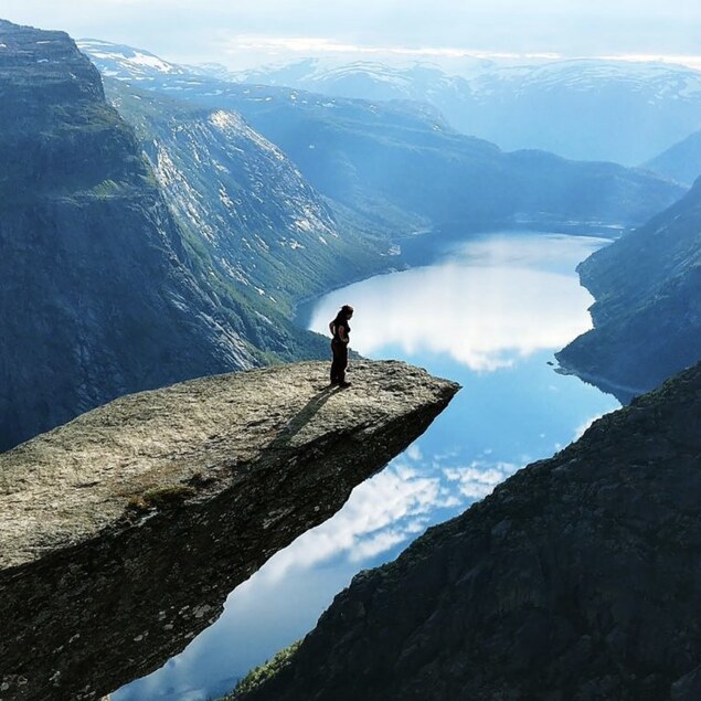 Une femme regarde vers le bas du haut d'un pic rocheux au-dessus d'une falaise à Trolltunga en Norvège.