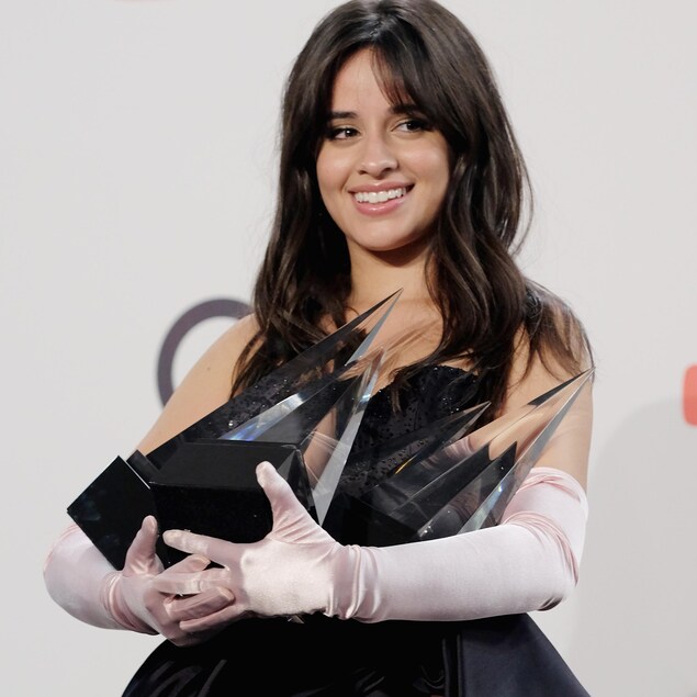 Camila Cabello, souriante, porte ses quatre trophées dans ses bras. Camila Cabello, souriante, porte ses quatre trophées dans ses bras.