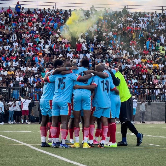 Des joueurs de soccer froment un caucus devant des gradins remplis.