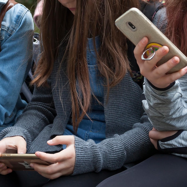 Des jeunes concentrés sur le contenu de leur cellulaire.