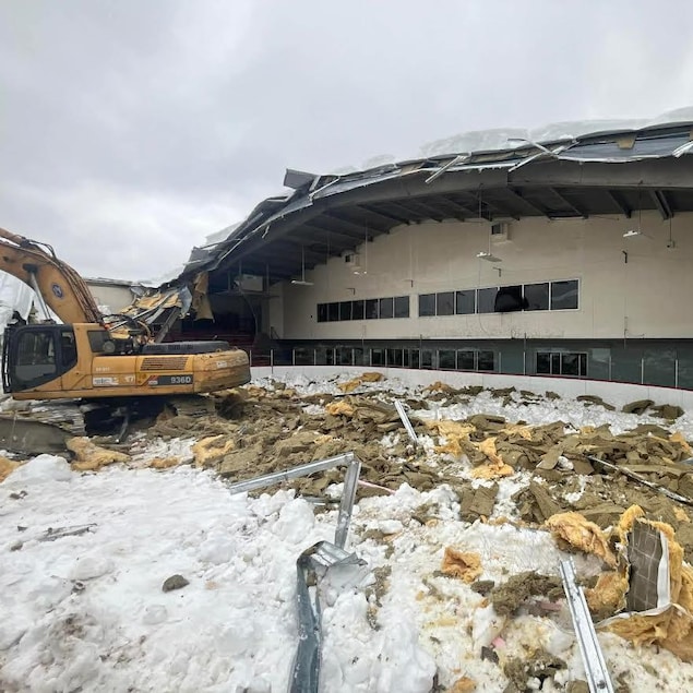 Une pelle mécanique sur les débris qui jonchent la patinoire de l'aréna d'Évain, devenu à ciel ouvert à cause de l'effondrement d'une partie du toit.