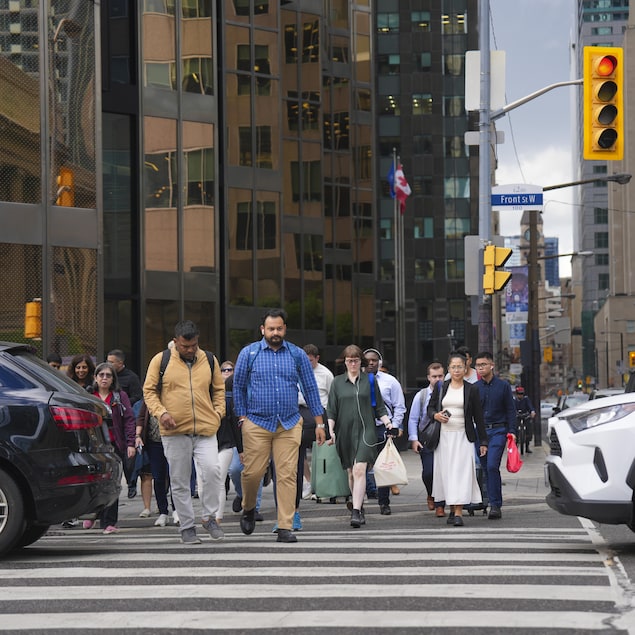 Des gens traversent une intersection du centre-ville de Toronto alors que des voitures bloquent une partie de la traverse piétonne. 