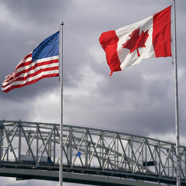 Les drapeaux des États-Unis et du Canada flottent devant un ciel sombre.