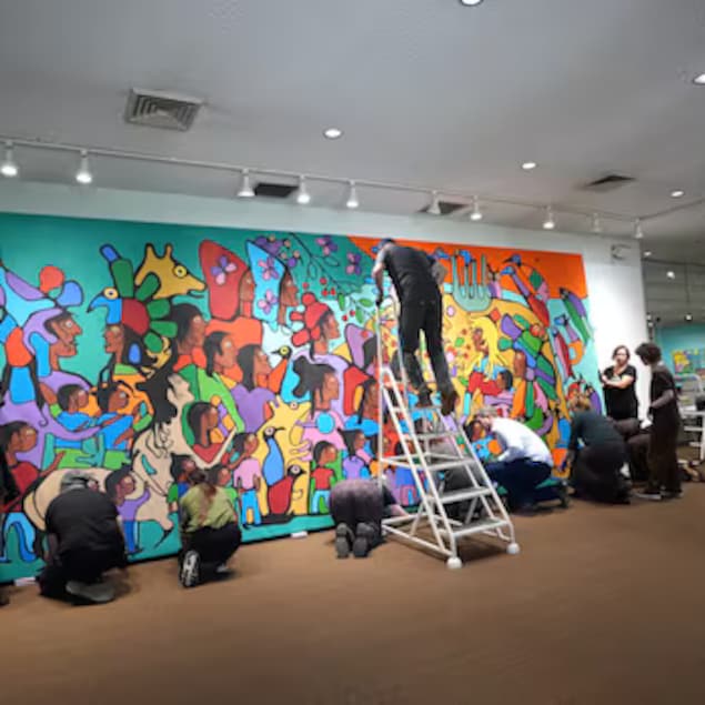 Un groupe de personnes, les unes debout, les autres à genoux, se tient face à une grande œuvre murale.