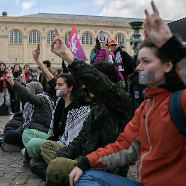 Des étudiants sont assis avec du ruban adhésif sur la bouche et une main dans les airs, sur la place du Panthéon à Paris.