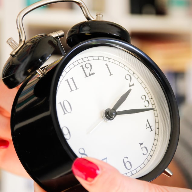 Une femme recule l'heure d'une horloge.