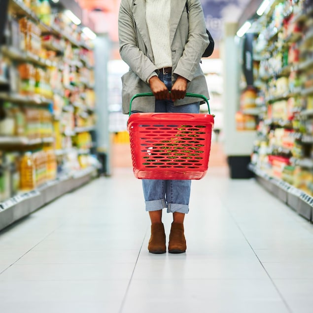 Une personne tient un panier d'épicerie dans une allée d'un supermarché.